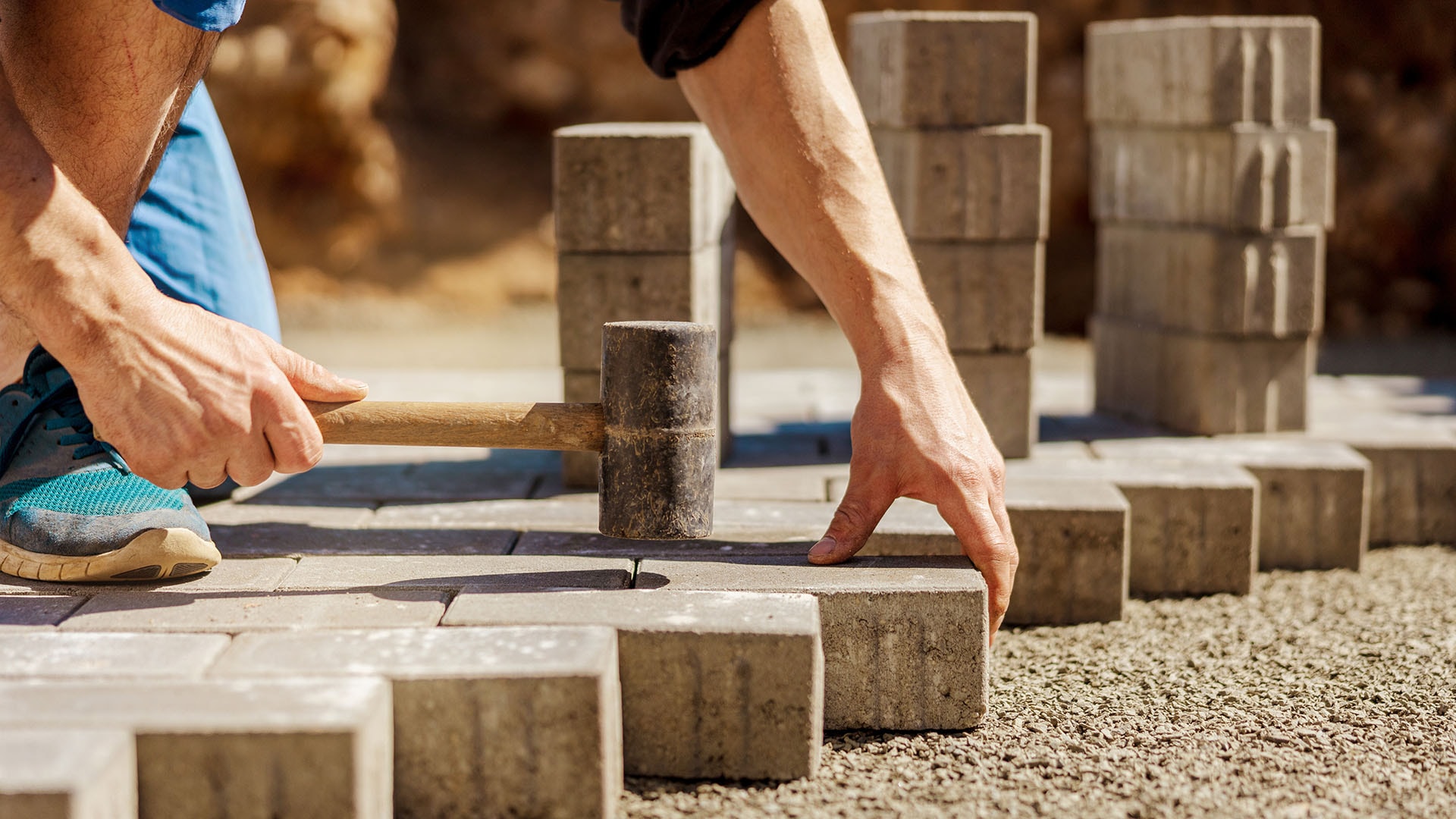 1920 mies asentaa harmaita pihakiviä paikoilleen käyttäen apunaan kuminuijaa