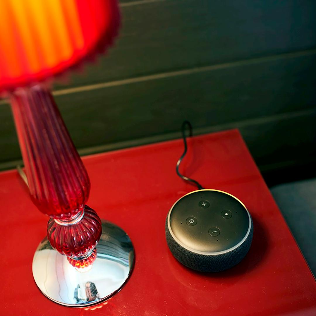 punainen pöytälamppu punaisella pöydällä ja lampun vieressä on koko huoneen valaistuksen säätönappulat