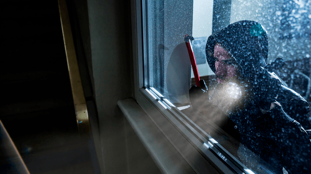 murtovaras kurkistaa pimeällä sisälle ja näyttää valoa lampullaan. kädessä sorkkarauta